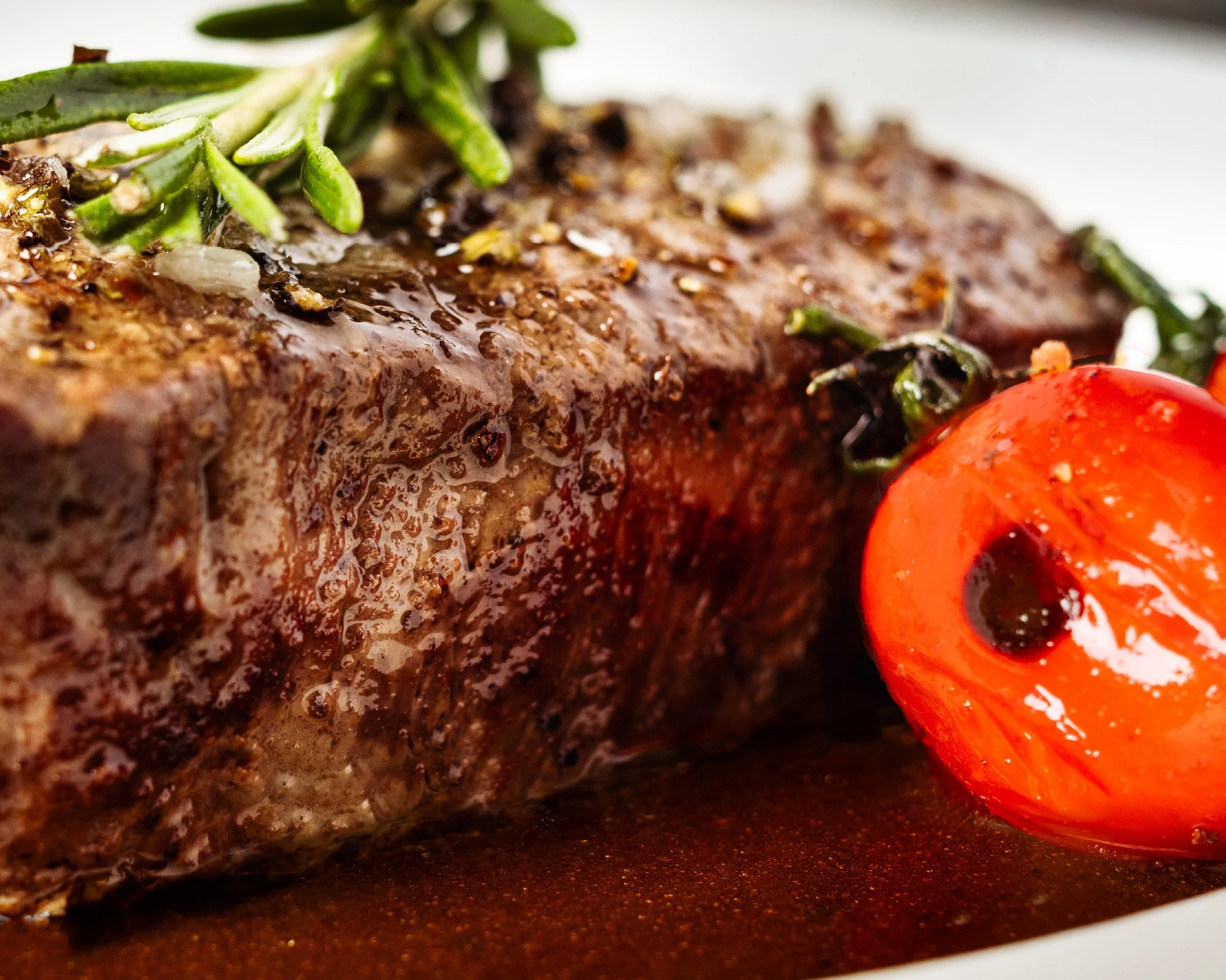 Close-up of a cooked steak garnished with fresh herbs and cherry tomato on the side.