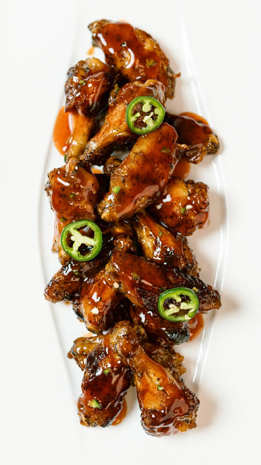 Barbecue chicken wings garnished with sliced jalapeños on a white plate