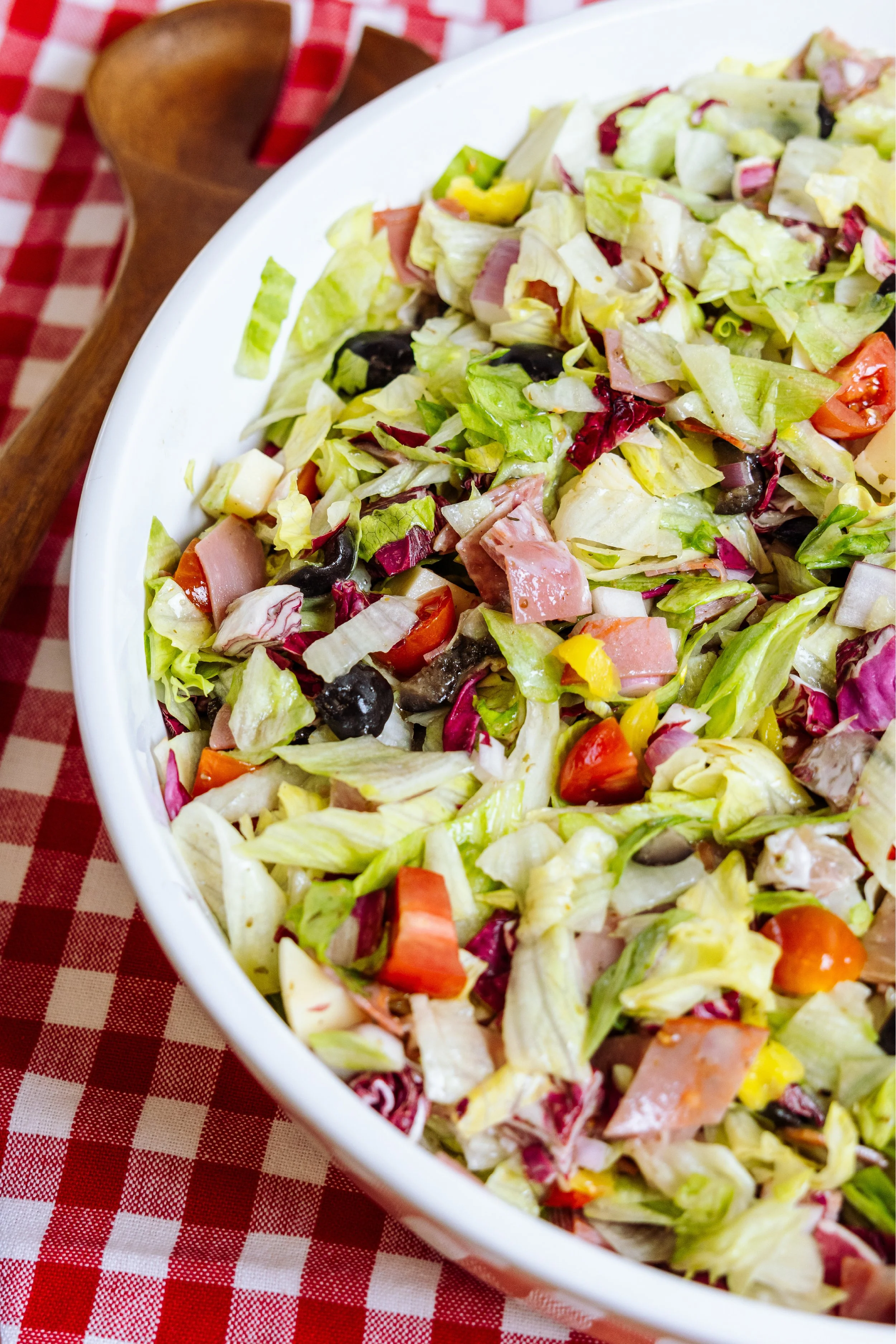 Fresh garden salad with lettuce, cherry tomatoes, cucumbers, and mixed vegetables served in a white dish on a red checkered tablecloth.