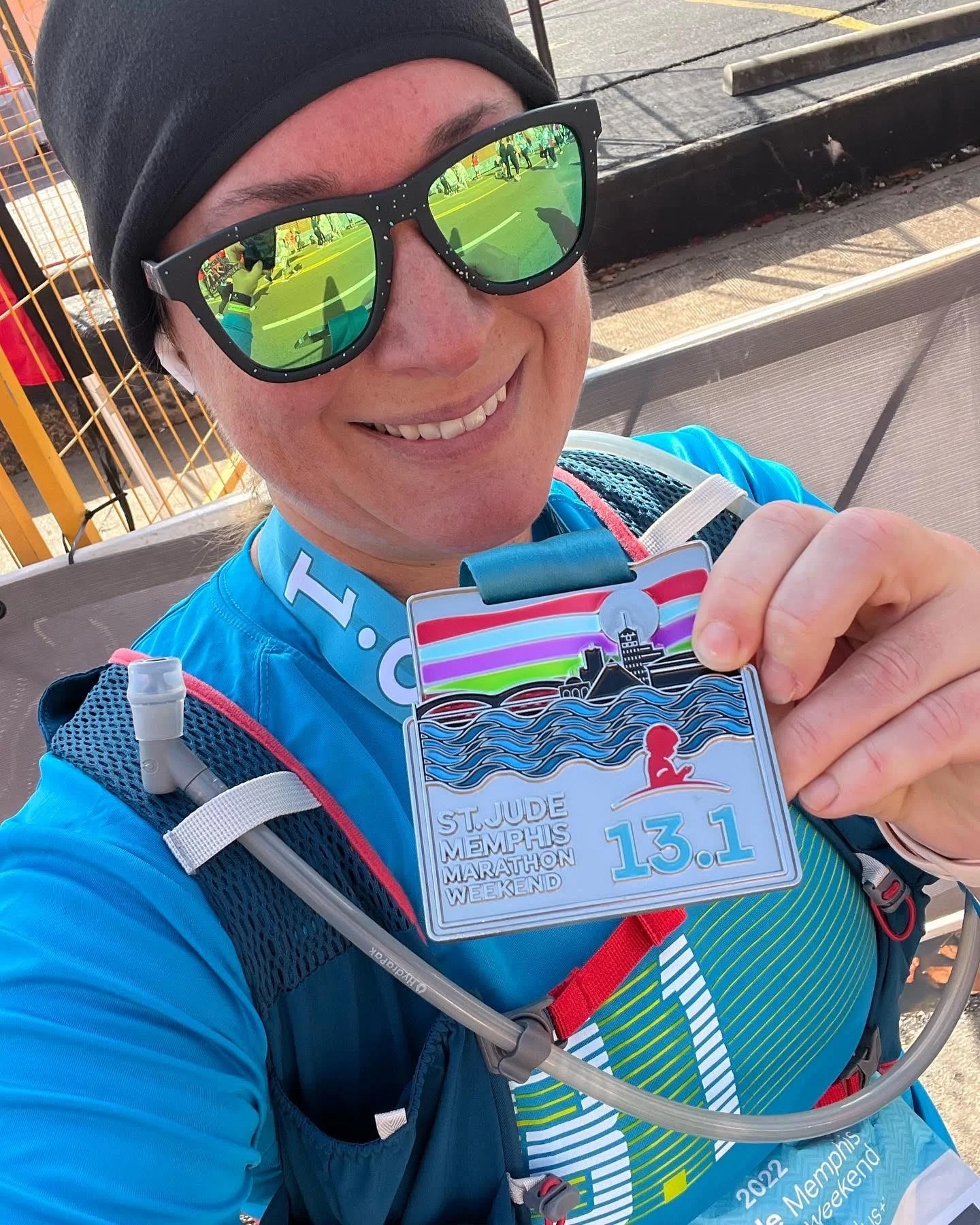 Woman smiling at camera and holding up her medal after running a half marathon