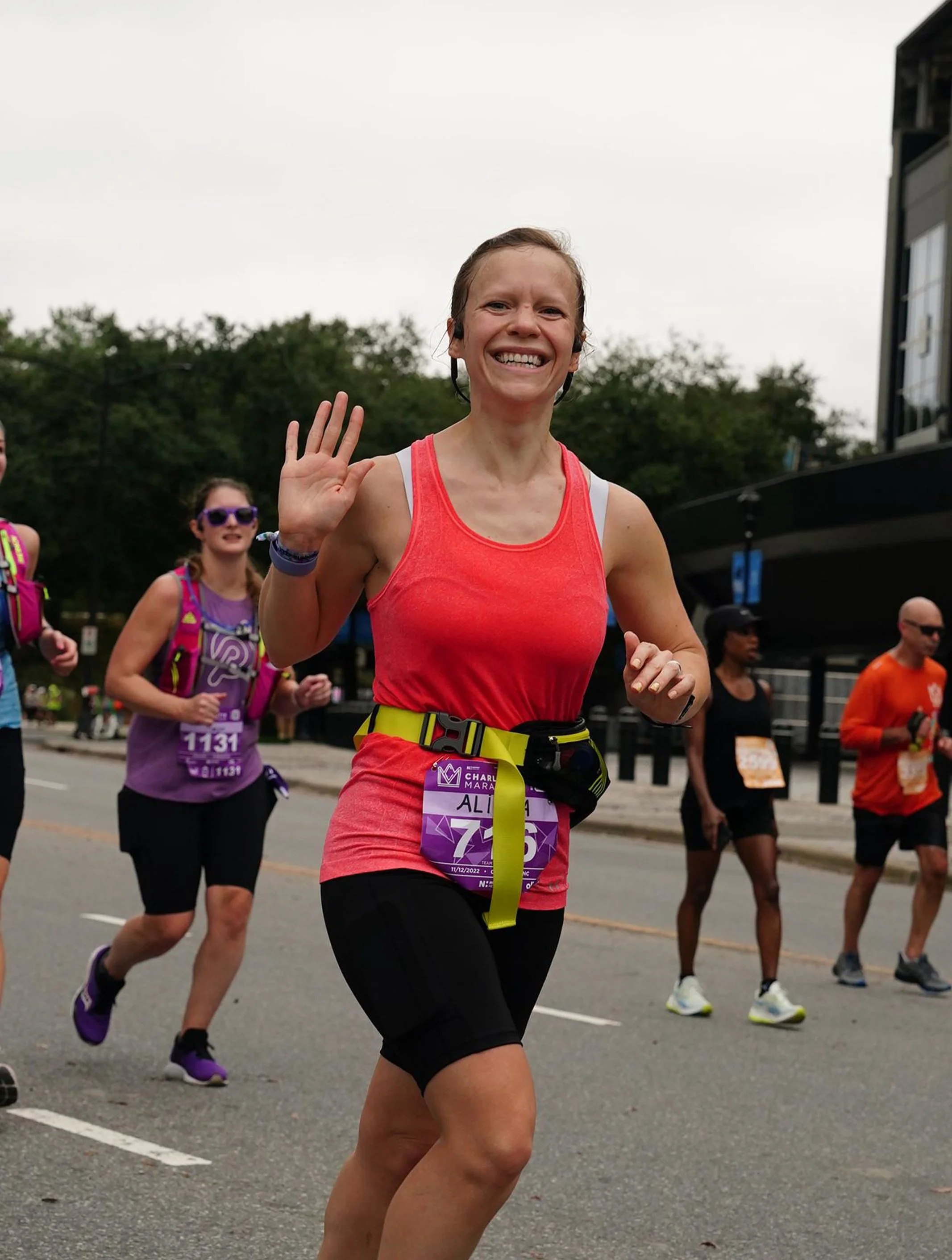 Woman in a pink tank top running the Charlotte marathon, waving at the camera