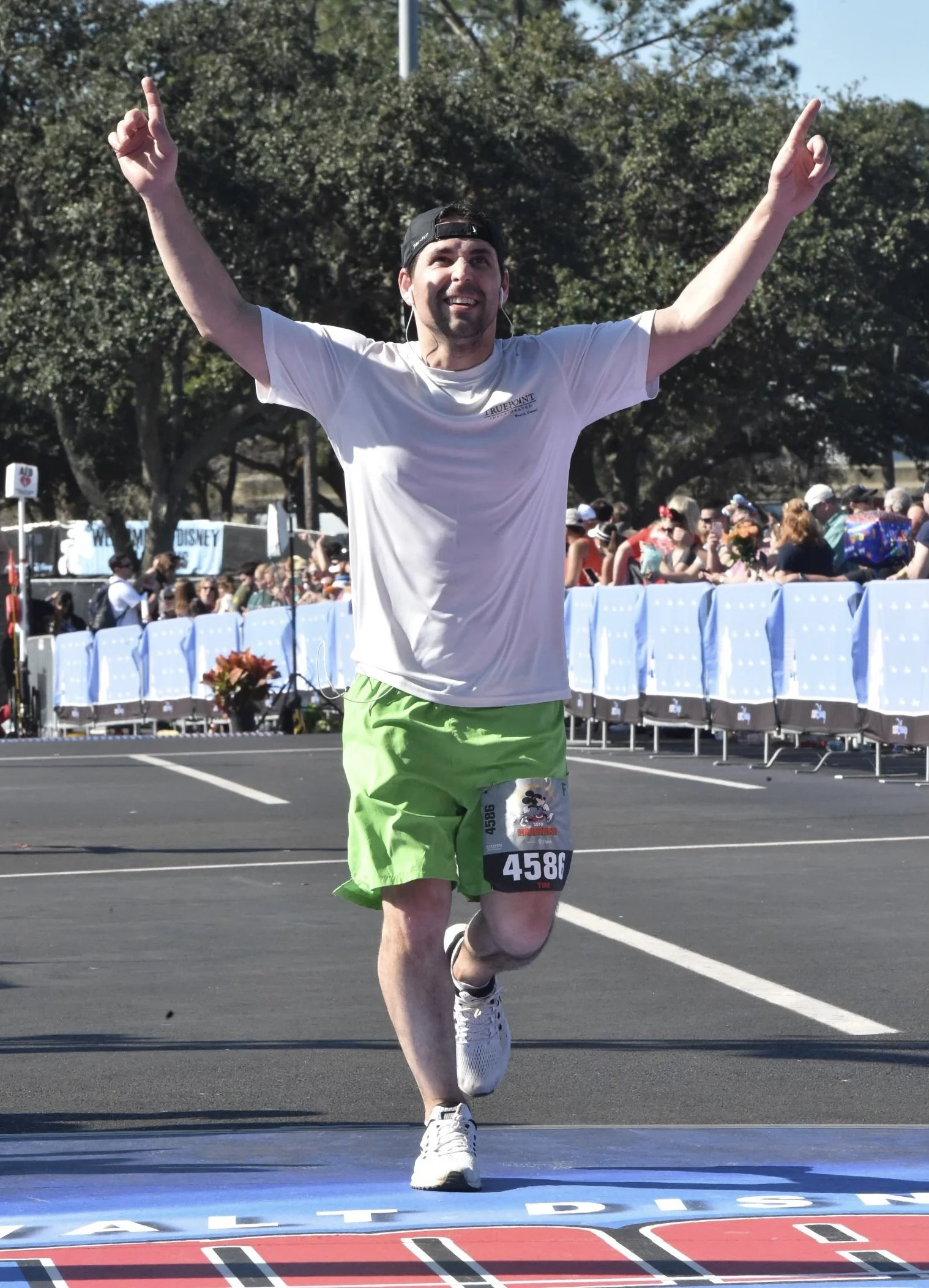 ManMale runner in white shirt and green shorts, raising his hands in victory as he crosses the finish line