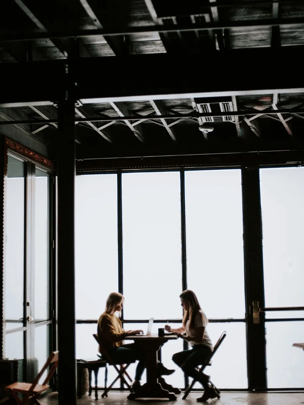 Two people working on laptops by a bright window, collaborative focus scene illustrating productivity with a time management coach.