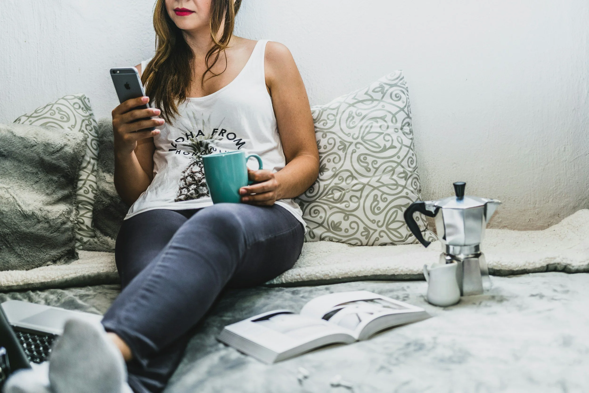 Online business coaching via Voxer and WhatsApp so support fits your schedule, woman entrepreneur on bed with phone, coffee mug, laptop, and book showing a relaxed business coaching service