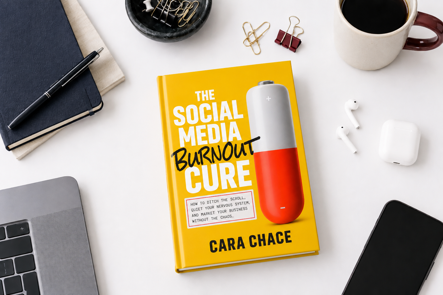The Social Media Burnout Cure by Cara Chace, a yellow book with a red and white battery, on a desk with coffee and a laptop