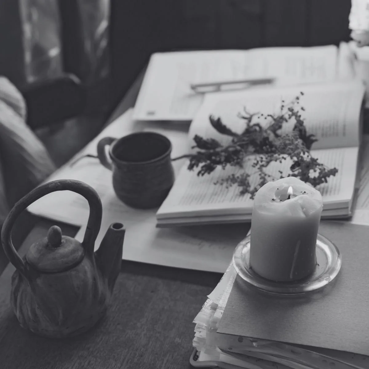 Black and white flat lay of a candle, tea kettle, and open books on a cozy home office desk
