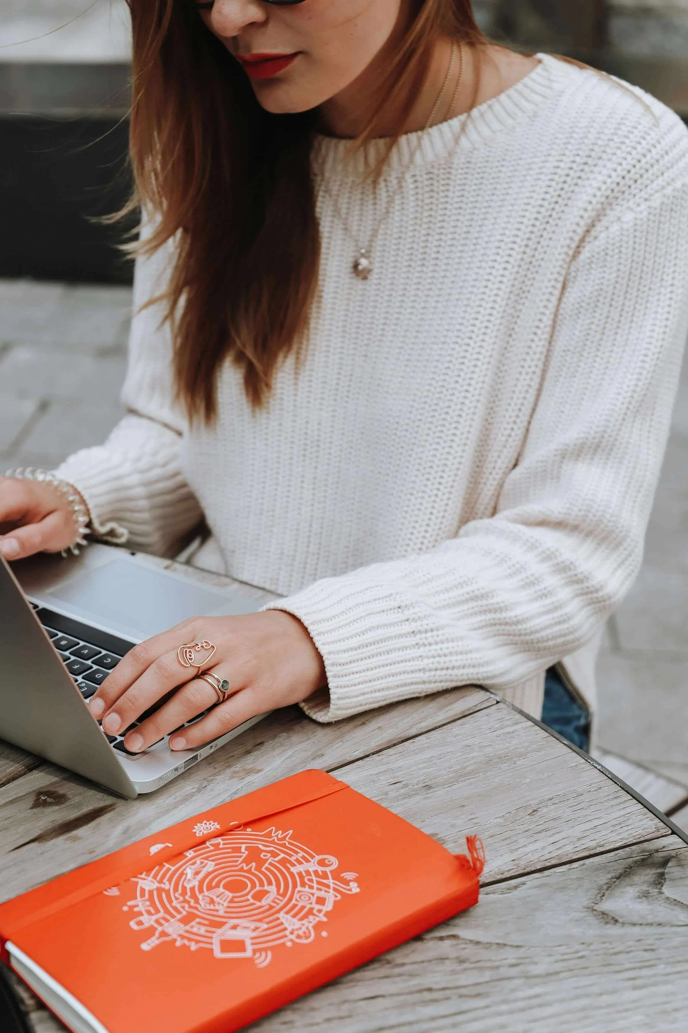 woman who's a busy entrepreneur in a cozy sweater on a laptop with an orange notebook, learning the benefits of a productivity coach