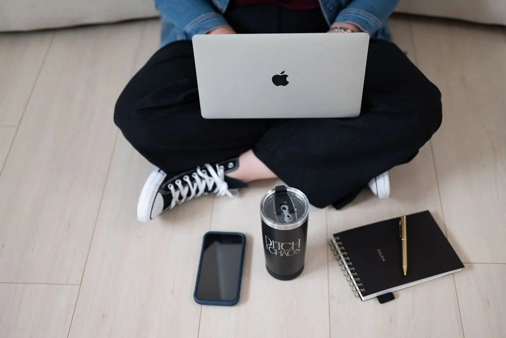 Cara Chace sitting on the floor with a laptop, smartphone, water bottle, and notebook.