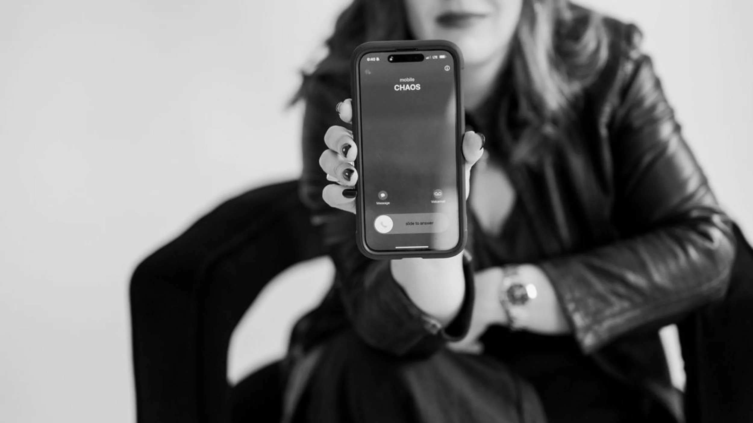 Cara Chace in black and phone brand photo holding a phone displaying a call from 'Chaos' to symbolize support with time management coaching