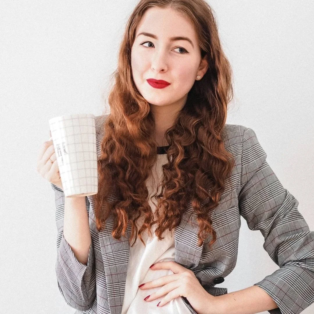 Confident woman entrepreneur in a blazer holding a coffee mug, looking thoughtfully upward — business coaching for women entrepreneurs.