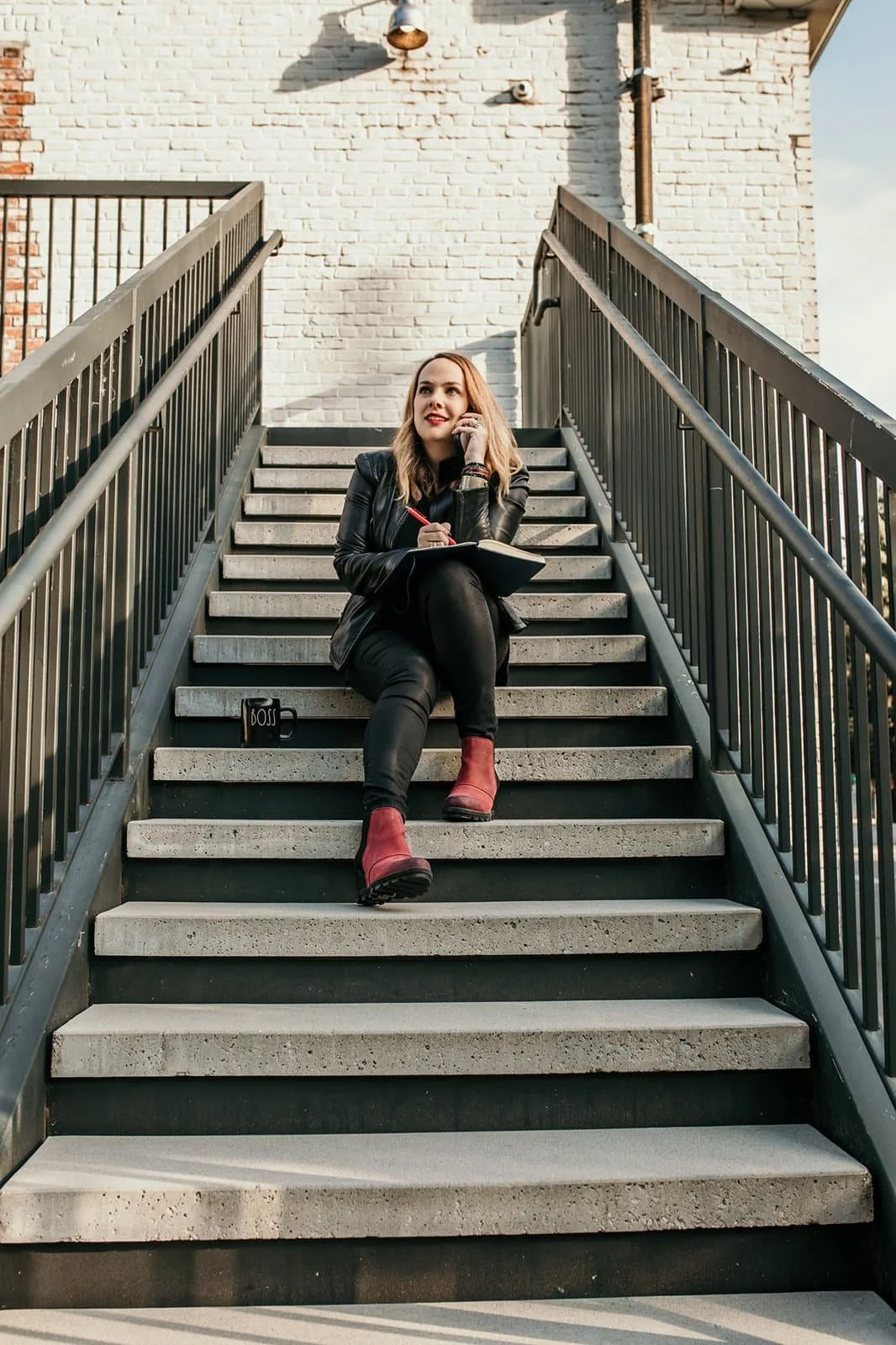 Cara Chace, Coach and Author, Conversation Starters for Press and Appearances on Podcasts, wearing all black sitting on steps talking on the phone with boss mug