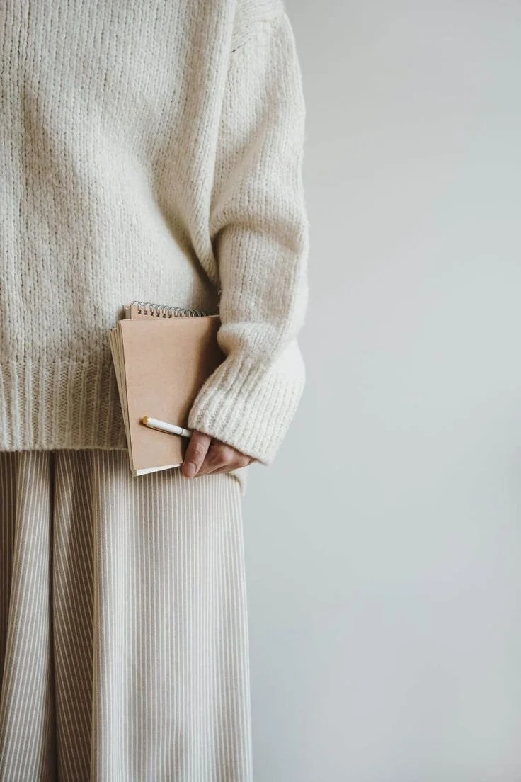 woman entrepreneur in a cozy off white outfit holding a notebook and pen, inspired by working with a time management coach