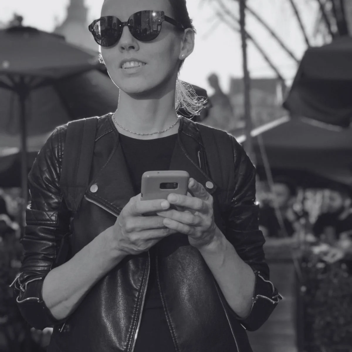 Black and white photo of a woman in sunglasses and a leather jacket checking her phone, for a post on Pinterest marketing