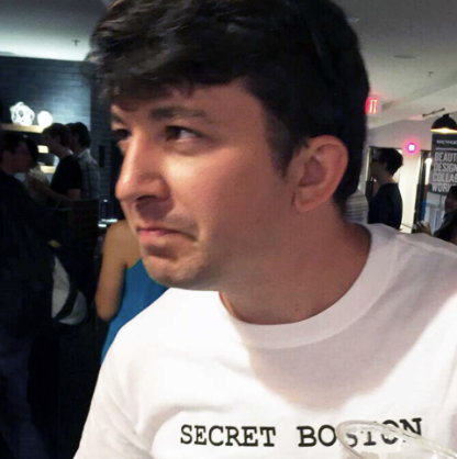 Man in a crowded venue wearing a "Secret Boston" t-shirt.