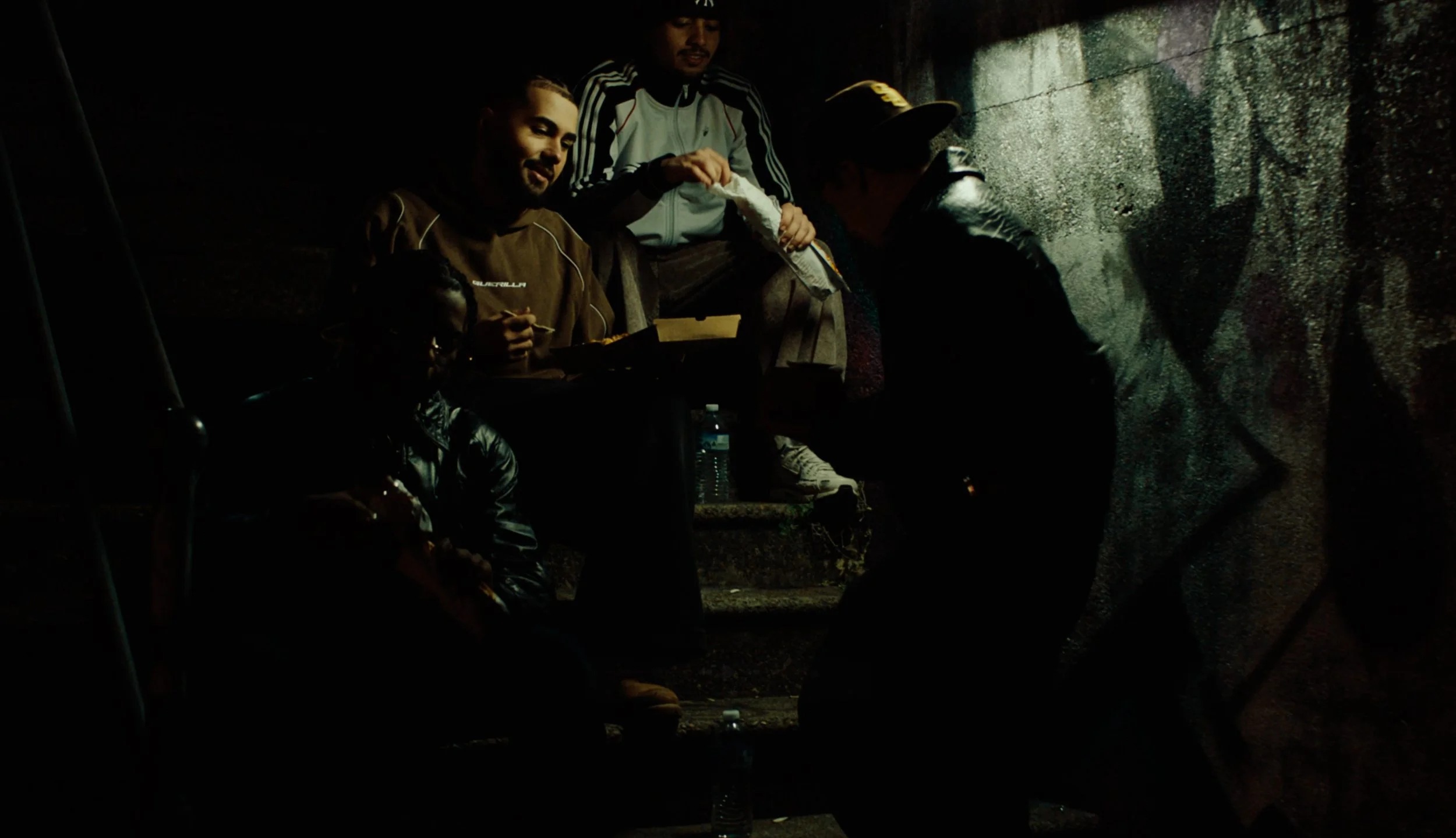 Screenshot from video campaign called Guerilla, directed by Nicholas Tan. Group of people sitting on outdoor stairs at night, some eating and conversation.