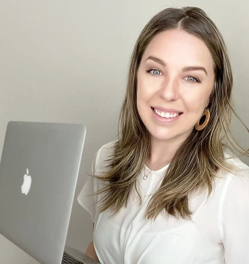 Katie Dunn, Owner of KStudio Design, A woman with shoulder-length brown hair, wearing a white top and large circular earrings, smiling at the camera while sitting in front of a silver Apple MacBook laptop.
