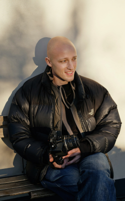 Man sitting on bench smiling holding a camera. Cancer depression therapist Pennsylvania Sarah Bryski-Hamrick