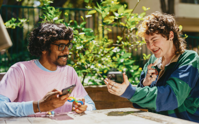 Two people sitting at a table outside looking at their phones, smiling together. Plants in background. Sarah Bryski-Hamrick, Therapist in Pennsylvania.