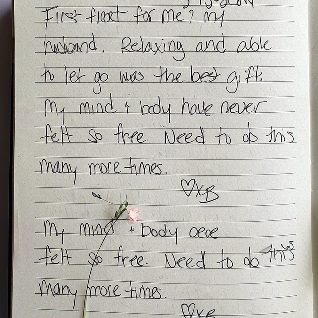 A handwritten note on lined paper with a small pink flower and a green stem placed on the page, partially obscuring some of the text.