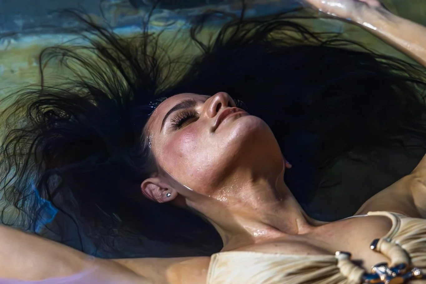 A woman with dark hair and closed eyes relaxing in a dark fluid, possibly during a spa treatment or artistic photo shoot.