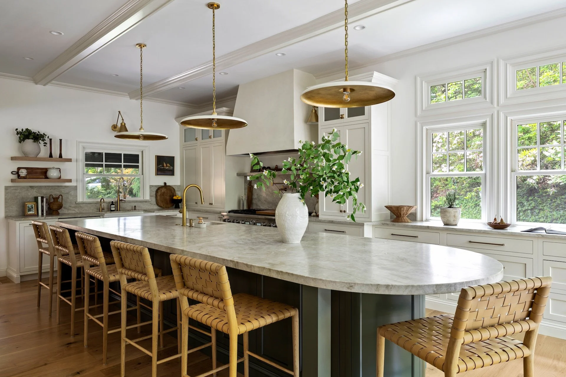 Elegant kitchen design featuring a long marble island, custom range hood, white cabinetry, brass fixtures, and warm wood floors