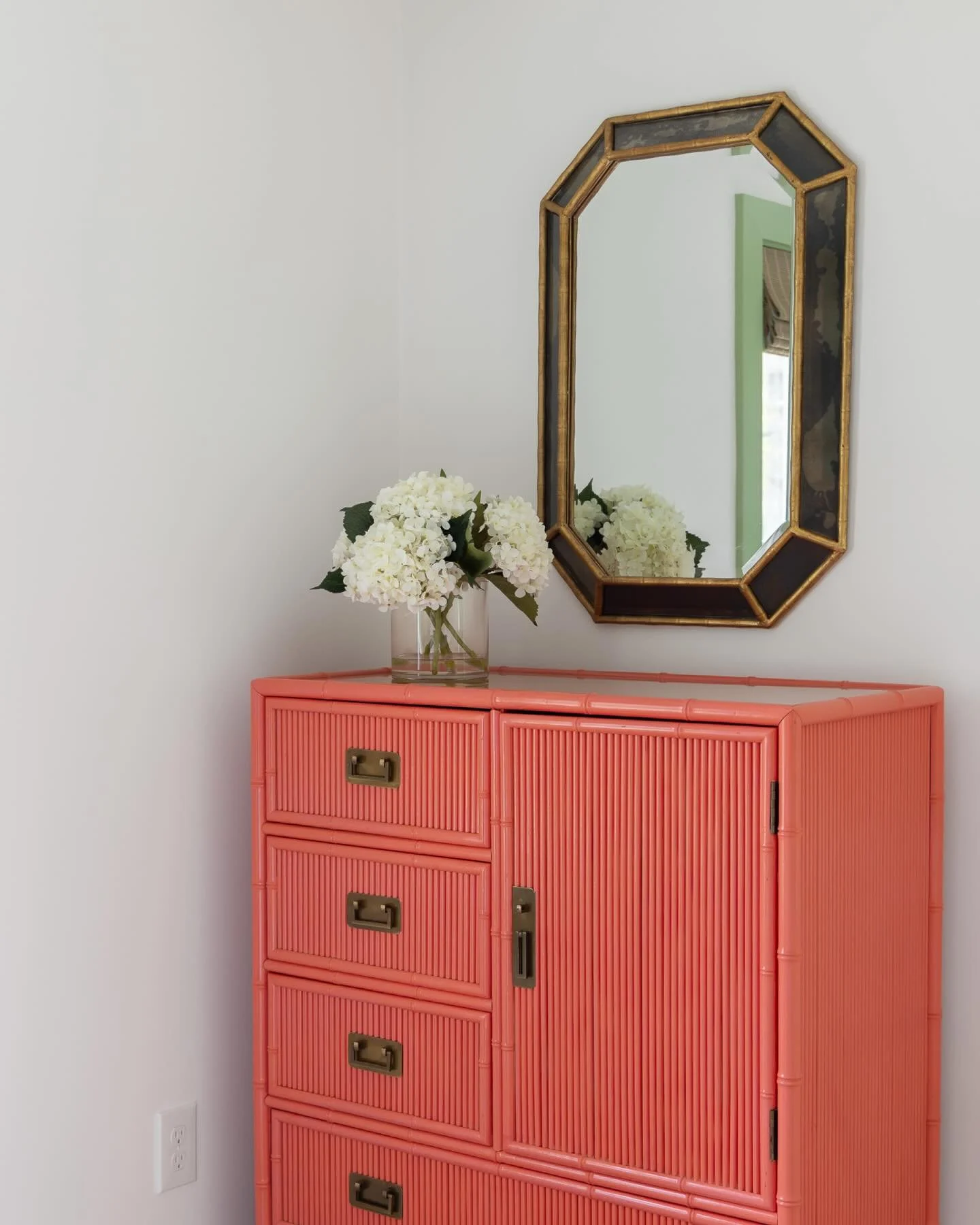 we love this sweet little corner in one of the guest rooms at the #preppyhollowhouse. a coat of coral paint transformed a vintage reeded cabinet into a perfect storage spot for guests. a brass and smoked glass mirror coordinates with the metal pulls 