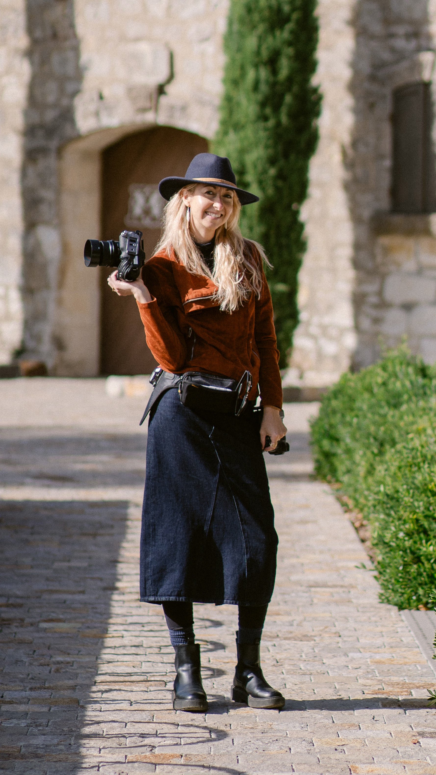 Michaela Joy standing outdoors holding a camera, offering 1:1 photography business coaching and strategic mentoring for professional photographers.