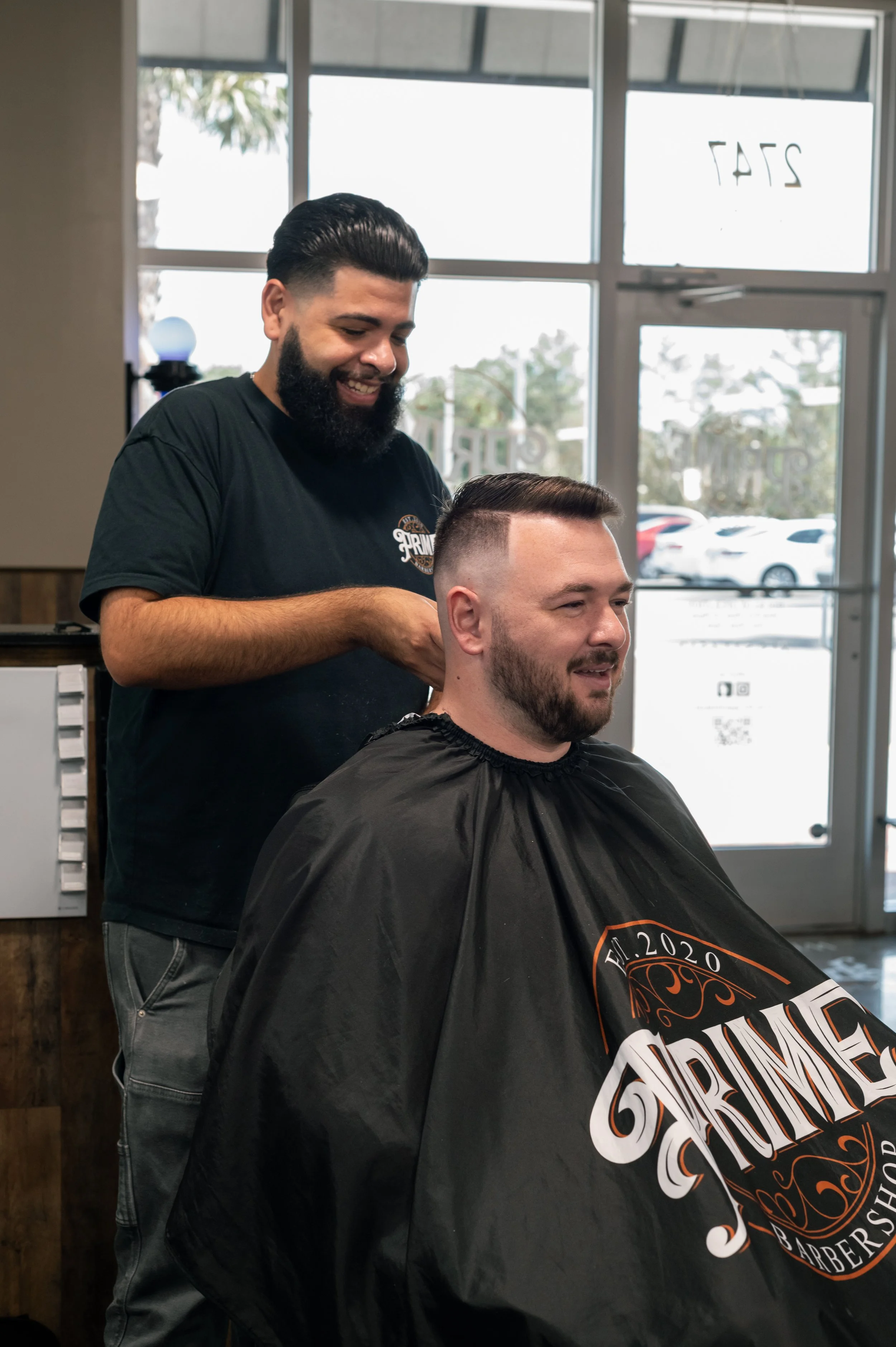 A man with a beard and slicked-back hair getting a haircut at a barbershop.