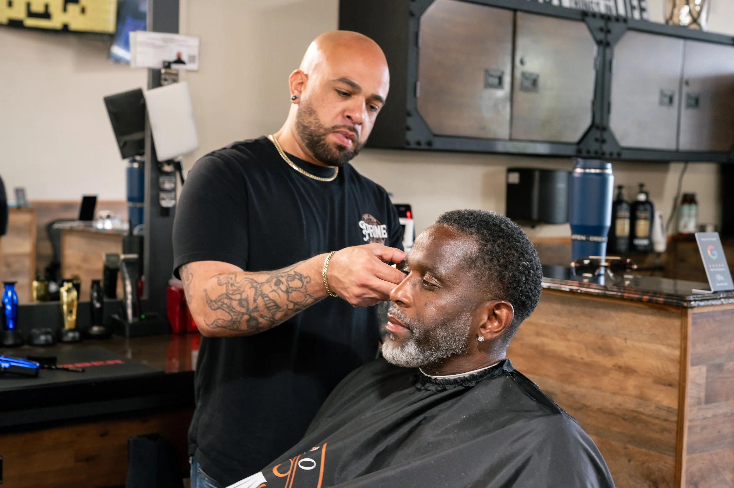 Barber trimming man's beard in barbershop.
