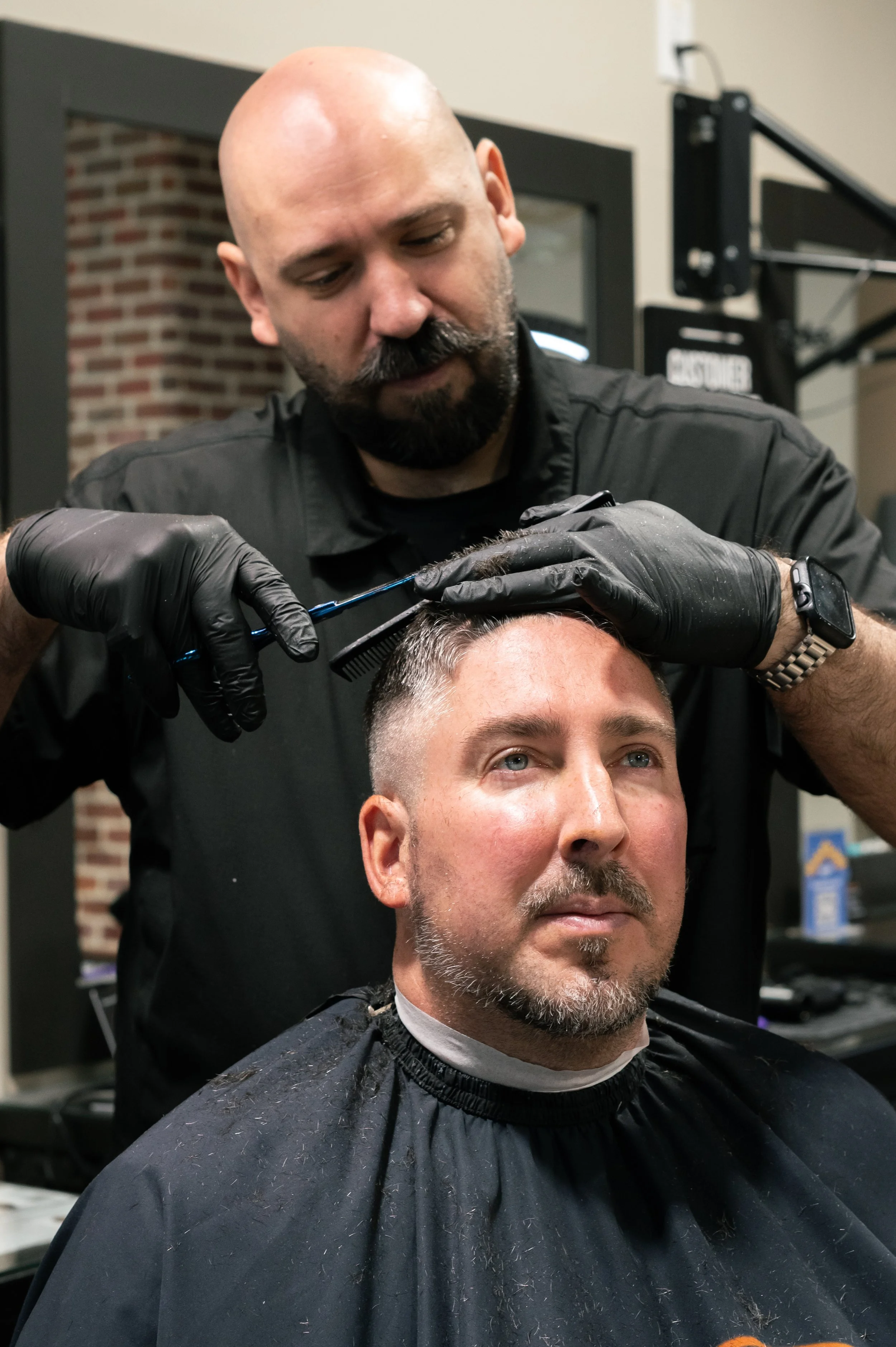 Barber in black gloves and uniform cutting a man's hair in a barber shop.