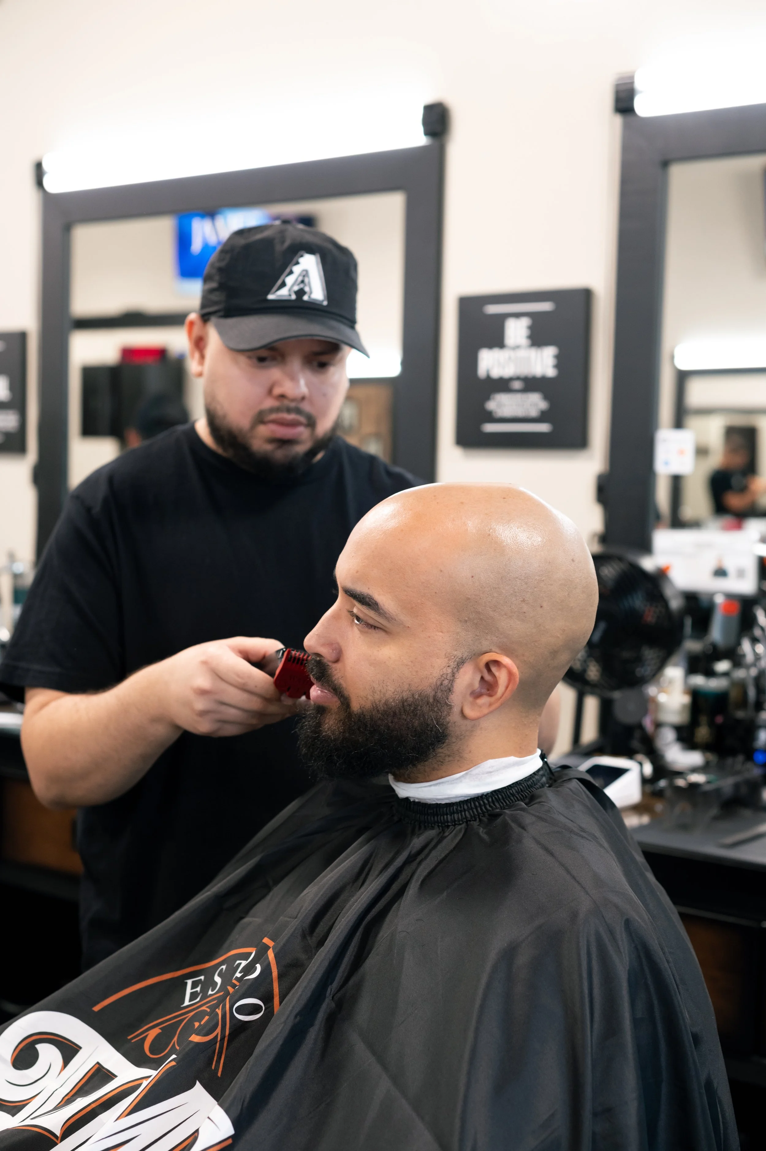 Barber trimming a man's beard in a barbershop with mirrors and hair styling tools in the background.