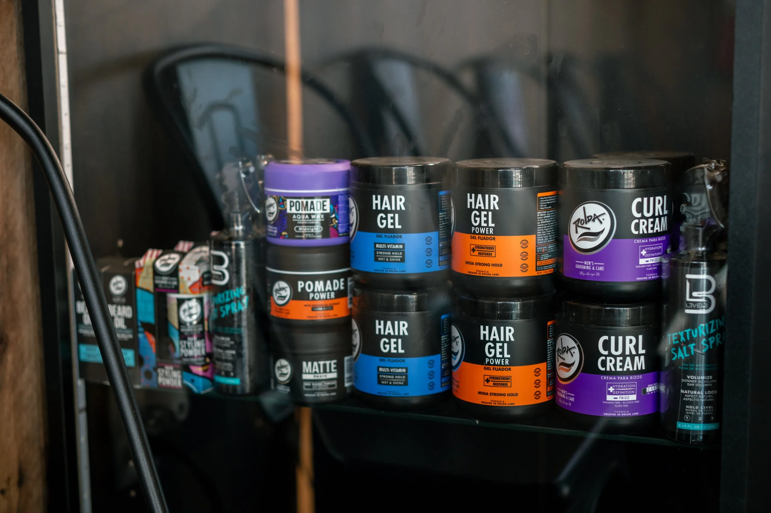 Shelf with various hair styling products including pomade, hair gel, and curl cream in black containers with colorful labels.