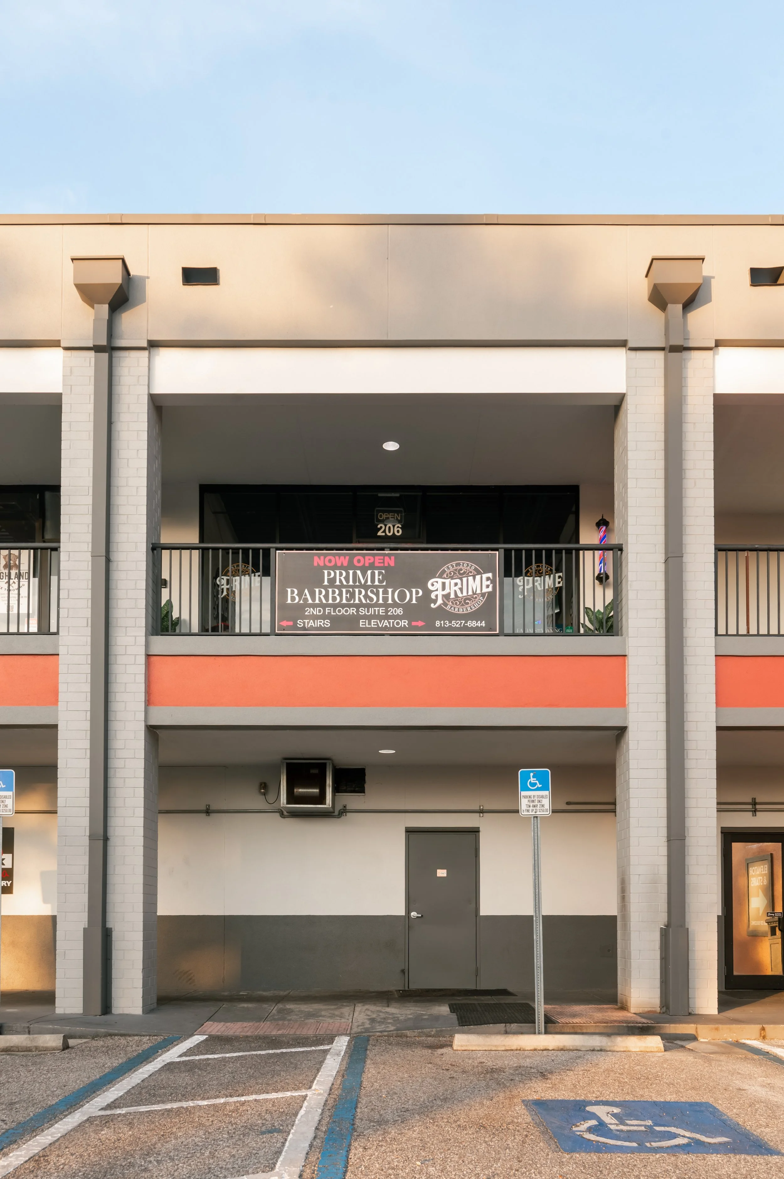 Parking lot with handicap parking space and entrance to a building with a sign for Prime Barbershop