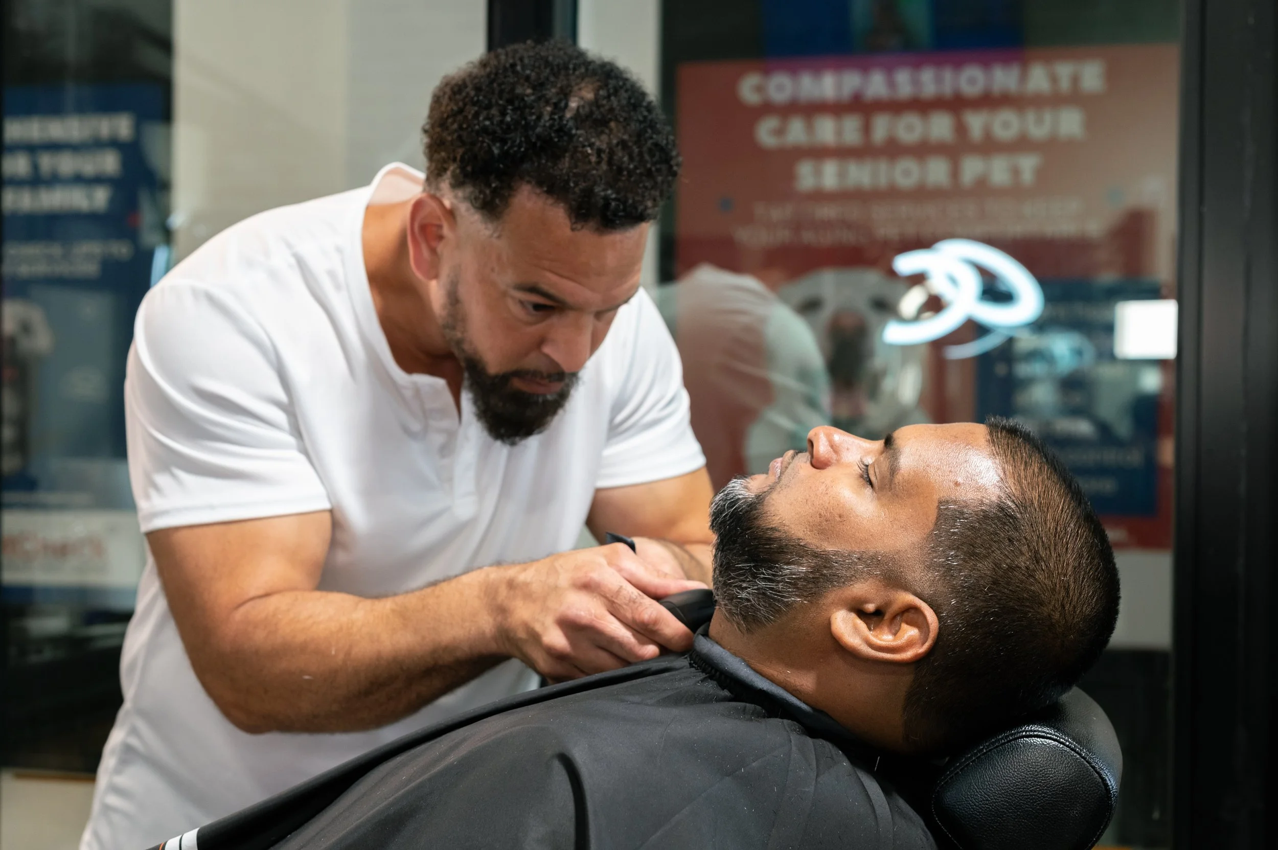 Barber trimming a man's beard at a barbershop.