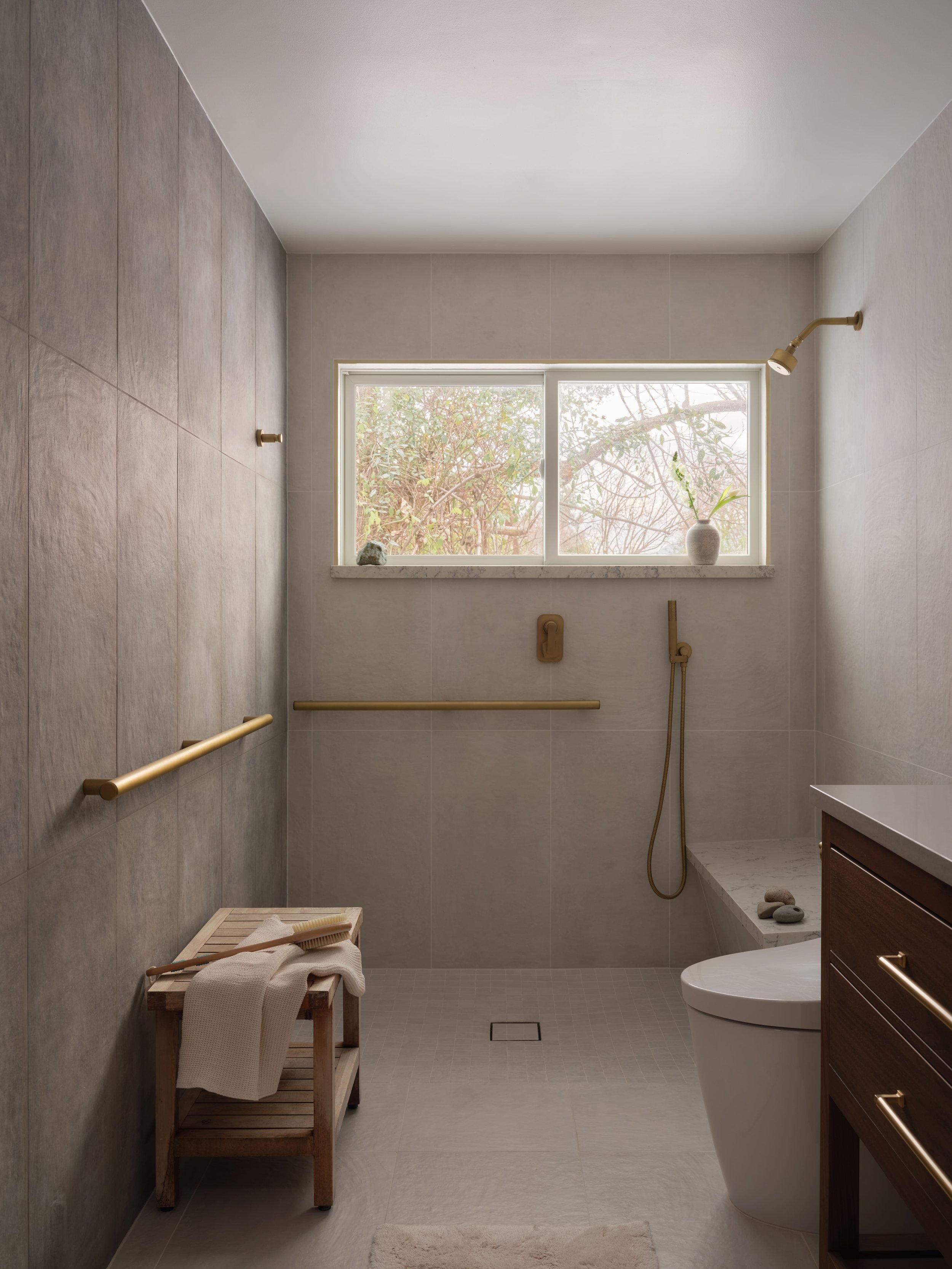 Zero-threshold roll-in shower with brass grab bars and teak shower bench, aging-in-place design in the Alamo Farmhouse (Jackson Way) pool house complete overhaul by Spearman Spaces