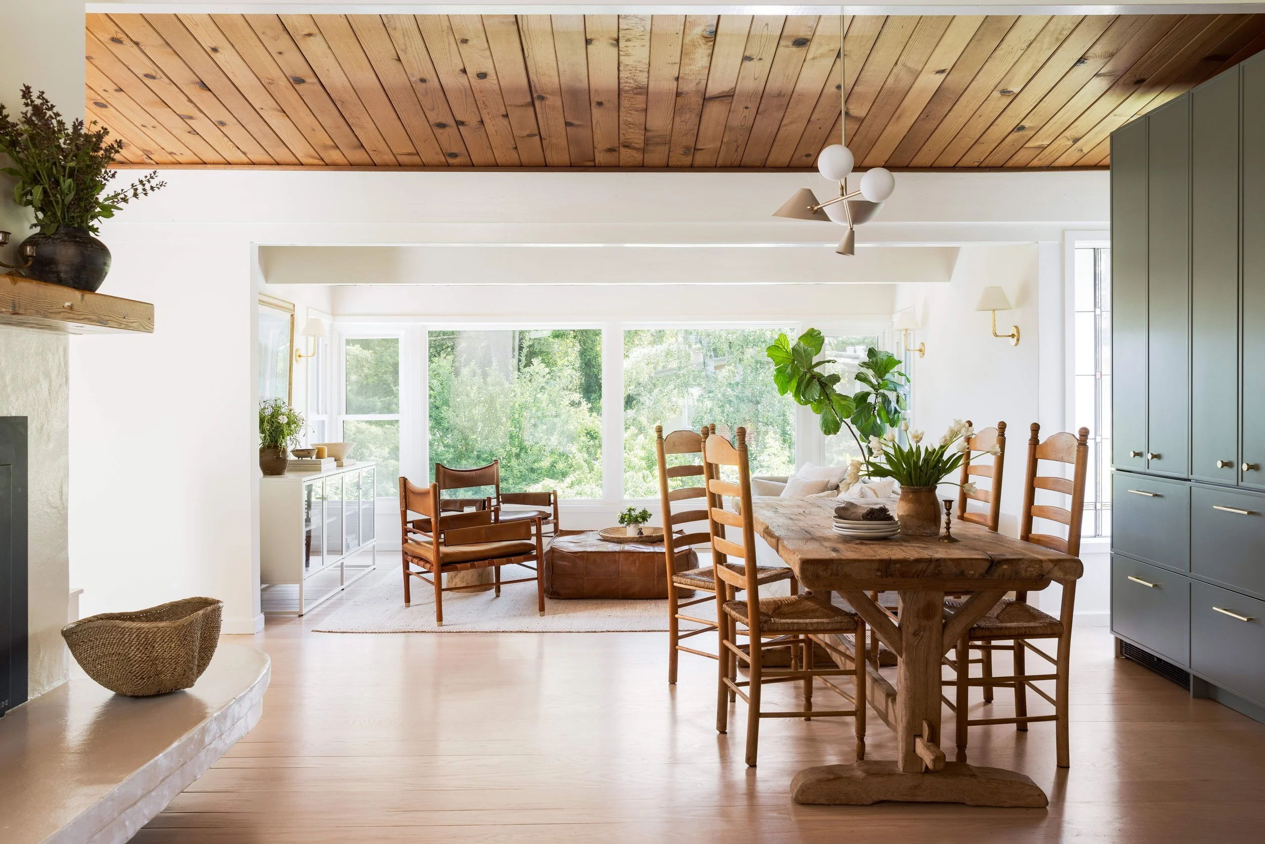 Open-concept dining and living area complete interior transformation with reclaimed wood table, ladder-back chairs, floor-to-ceiling windows, and stone fireplace hearth, Marin County Craftsman remodel by Spearman Spaces