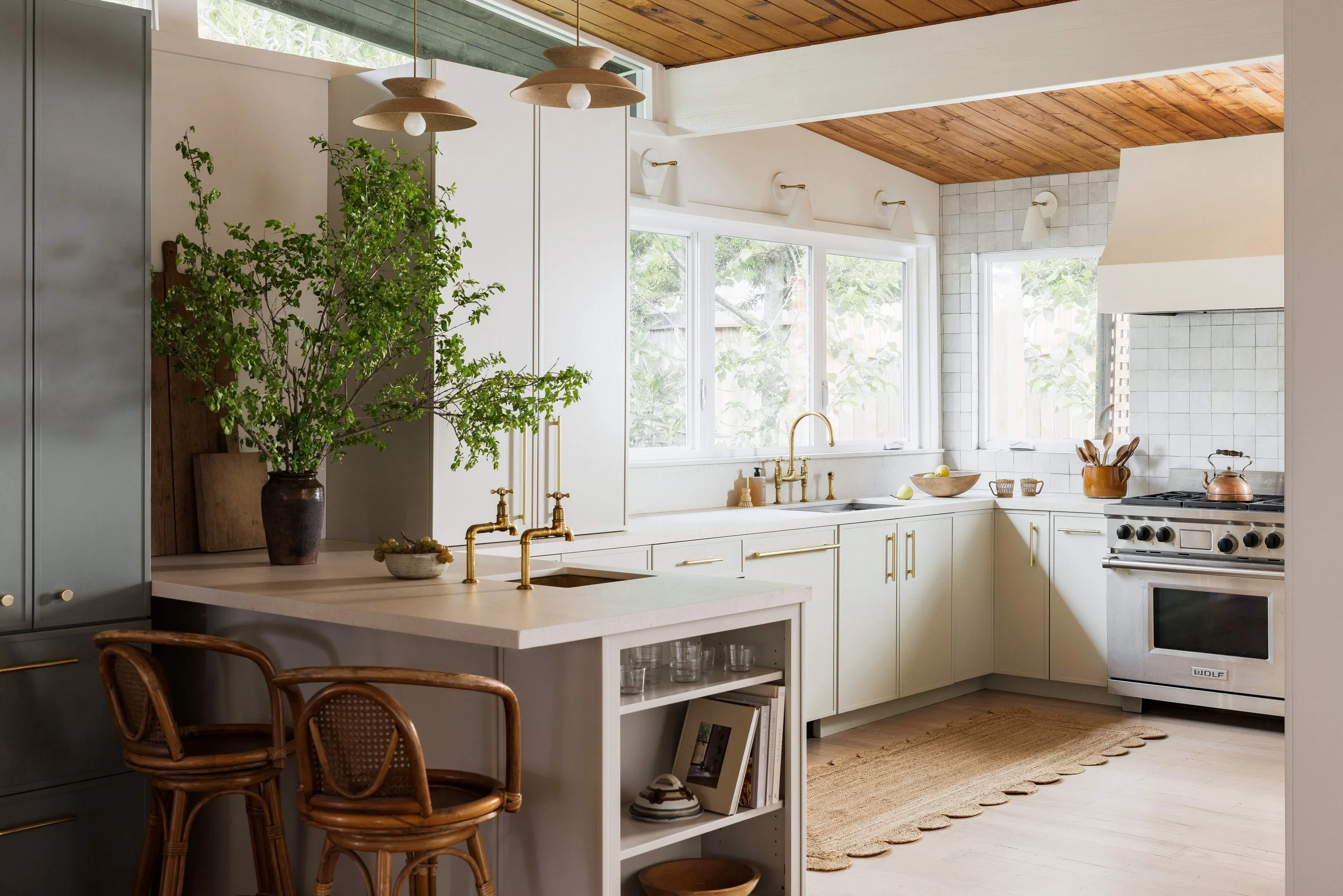 Kitchen hero with sage cabinetry, brass bridge faucet, white zellige tile, Wolf range, and wood-paneled ceiling, Marin County Craftsman interior architecture renovation by Spearman Spaces