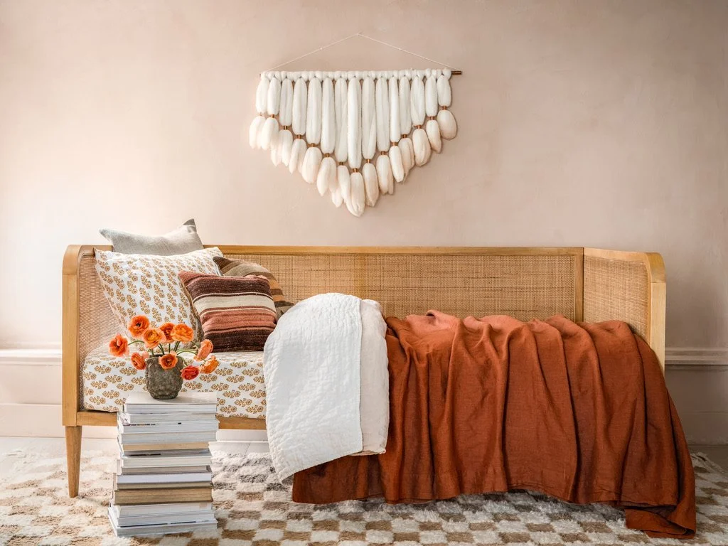 Styled daybed vignette with rattan cane-back frame, layered rust and cream textiles, and a fringed wall hanging, in the San Francisco Craftsman Victorian gut renovation by Spearman Spaces