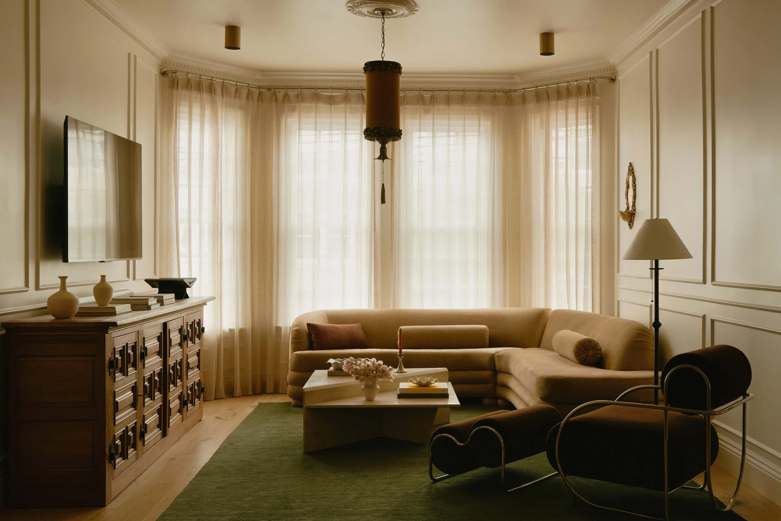 Crafstman style living room with a curved beige velvet sofa, dark leather and chrome accent chairs, a carved wood sideboard, ornate ceiling medallion, historic restoration & modernization by Spearman Spaces