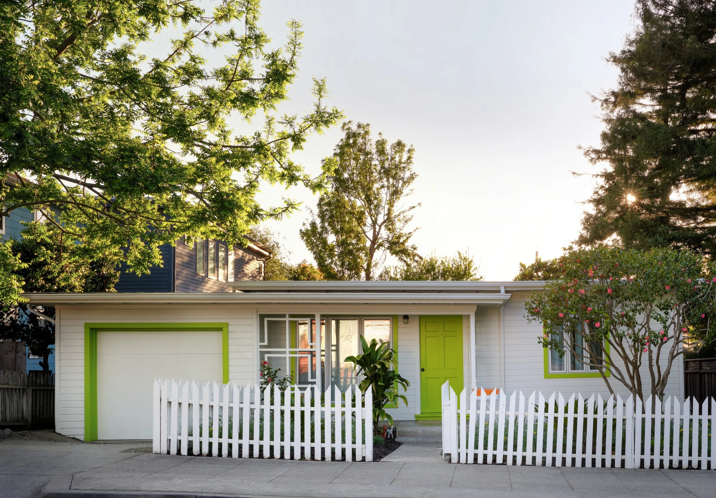 Entire-home remodel single-story California Ranch exterior with lime green door, garage, and window trim, white picket fence, and mature landscaping including blooming camellias, California Ranch comprehensive renovation by Spearman Spaces