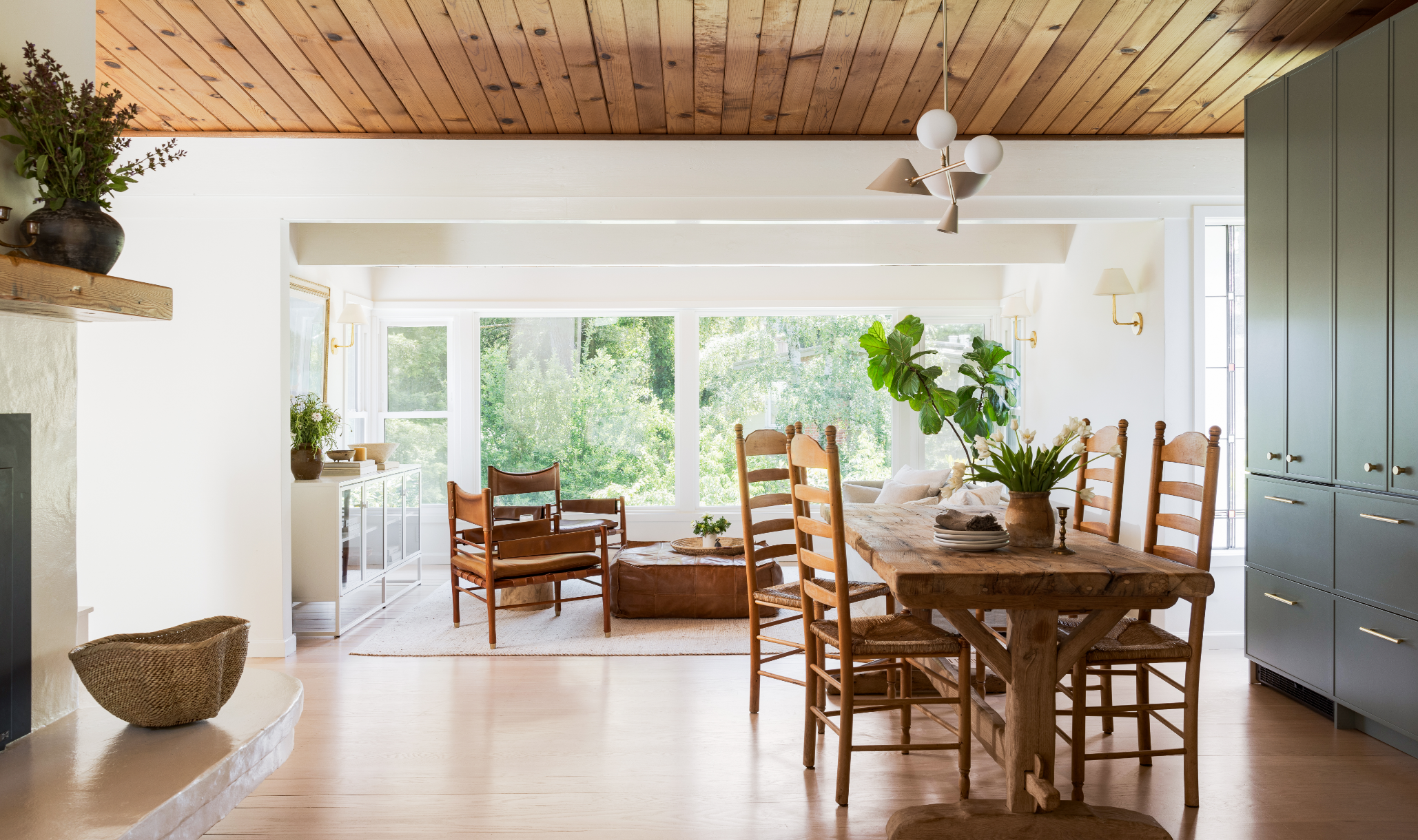 Open-concept dining and living area transformation with reclaimed wood table, ladder-back chairs, floor-to-ceiling windows, and stone fireplace hearth, Marin County Craftsman complete furnishing and interior architecture remodel by Spearman Spaces