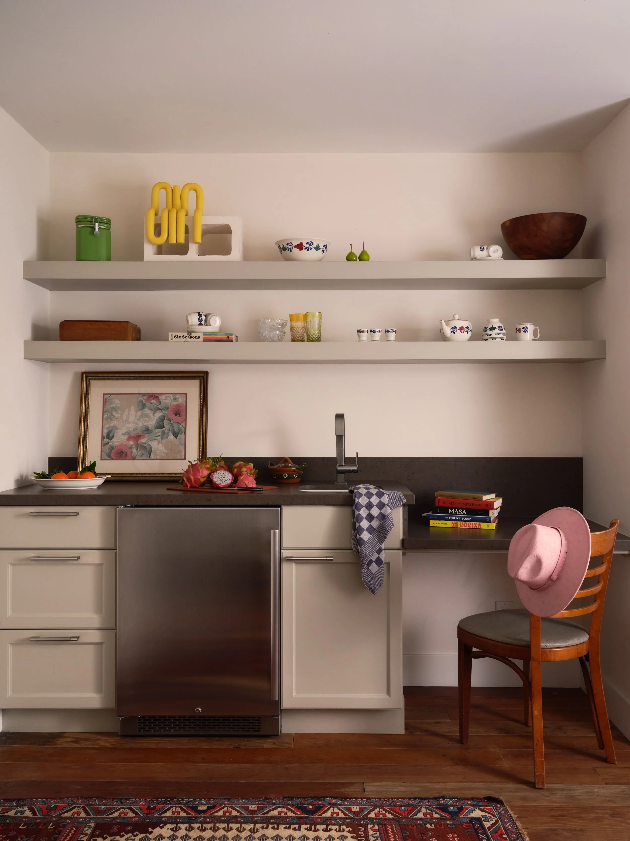 Pool house kitchenette with open shelving, mini fridge, wicker chair, and a pink hat, styled with dragon fruit and citrus, Alamo Farmhouse (Jackson Way) whole-home transformation by Spearman Spaces
