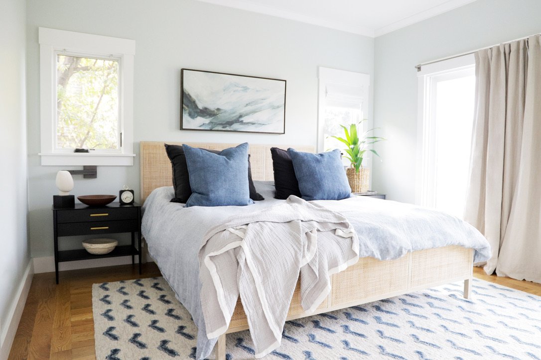 Primary bedroom hero with cane headboard, blue and black pillows, black nightstand, and abstract landscape art, Oakland Bungalow (61st Street) whole-home remodel by Spearman Spaces