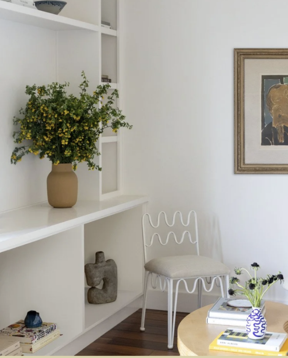 Custom architectural redesign built-in white shelving, ceramic vase of yellow wildflowers, beside a wavy wire-frame chair with cream cushion, in a living room,Transitional Italianate remodel (De Haro Street, Potrero Hill)