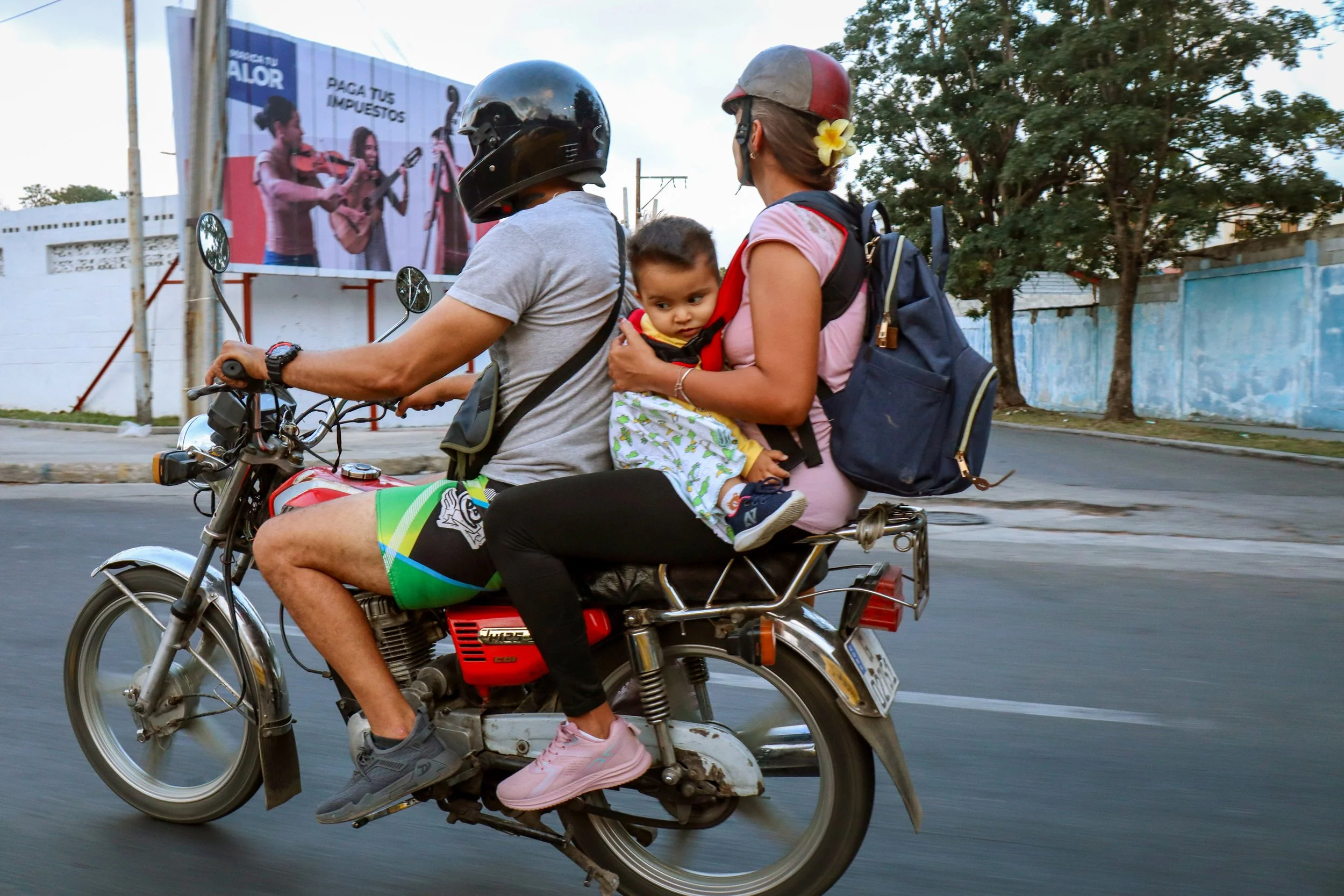 HAVANA, CUBA — March 7, 2026: A young child sits on a motorcycle between two adults, likely parents, on a Havana street. As fuel shortages persist, many Cubans have turned to motorcycles, scooters, and other alternative vehicles.