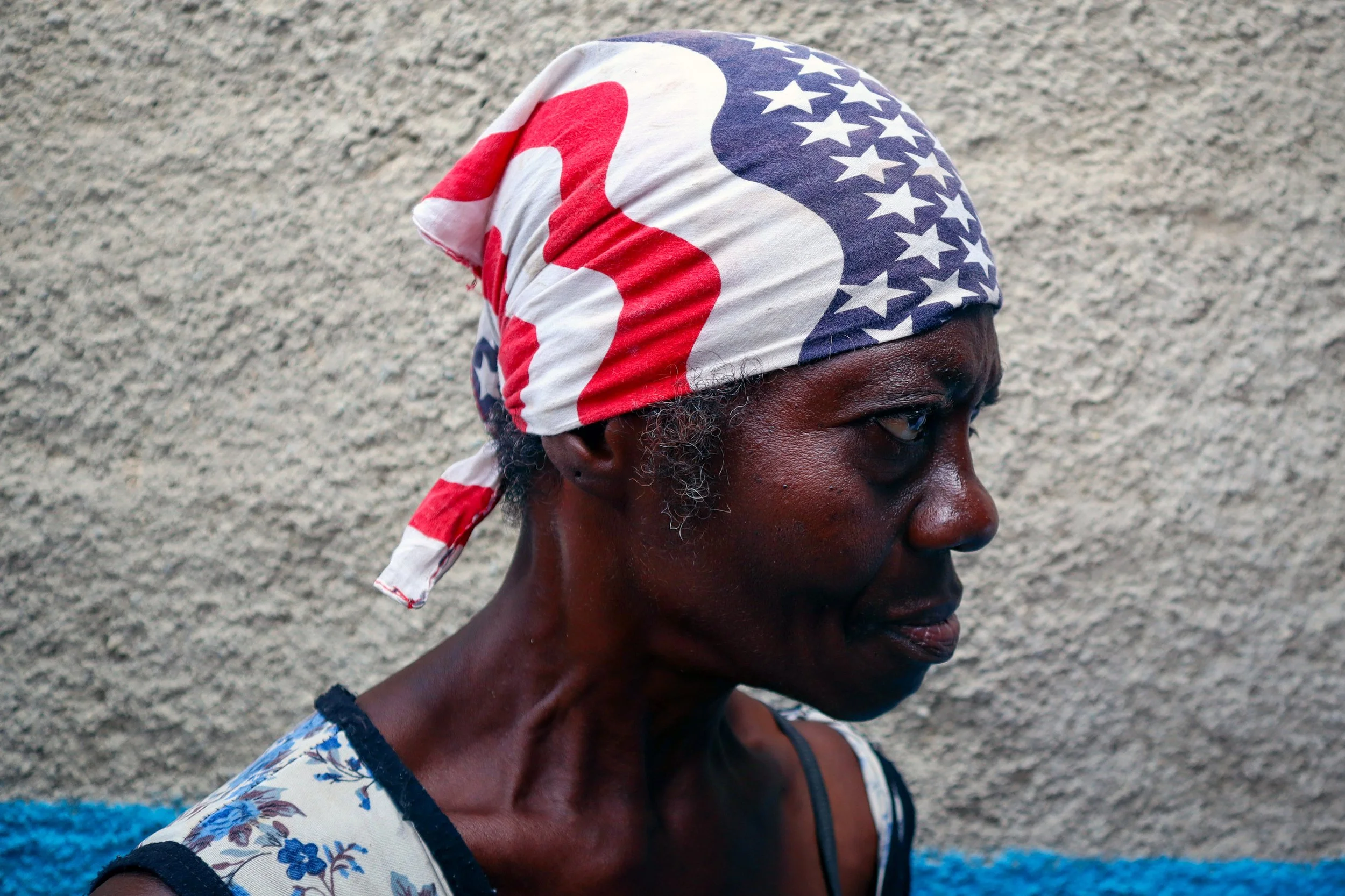 HAVANA, CUBA — March 8, 2026: Angela Daudinot Baro wears a USA bandana in La Güinera as she waits to eat a meal prepared by Iliana Macias Pulido, known as “Mama,” and her team, while others wait nearby for food. 