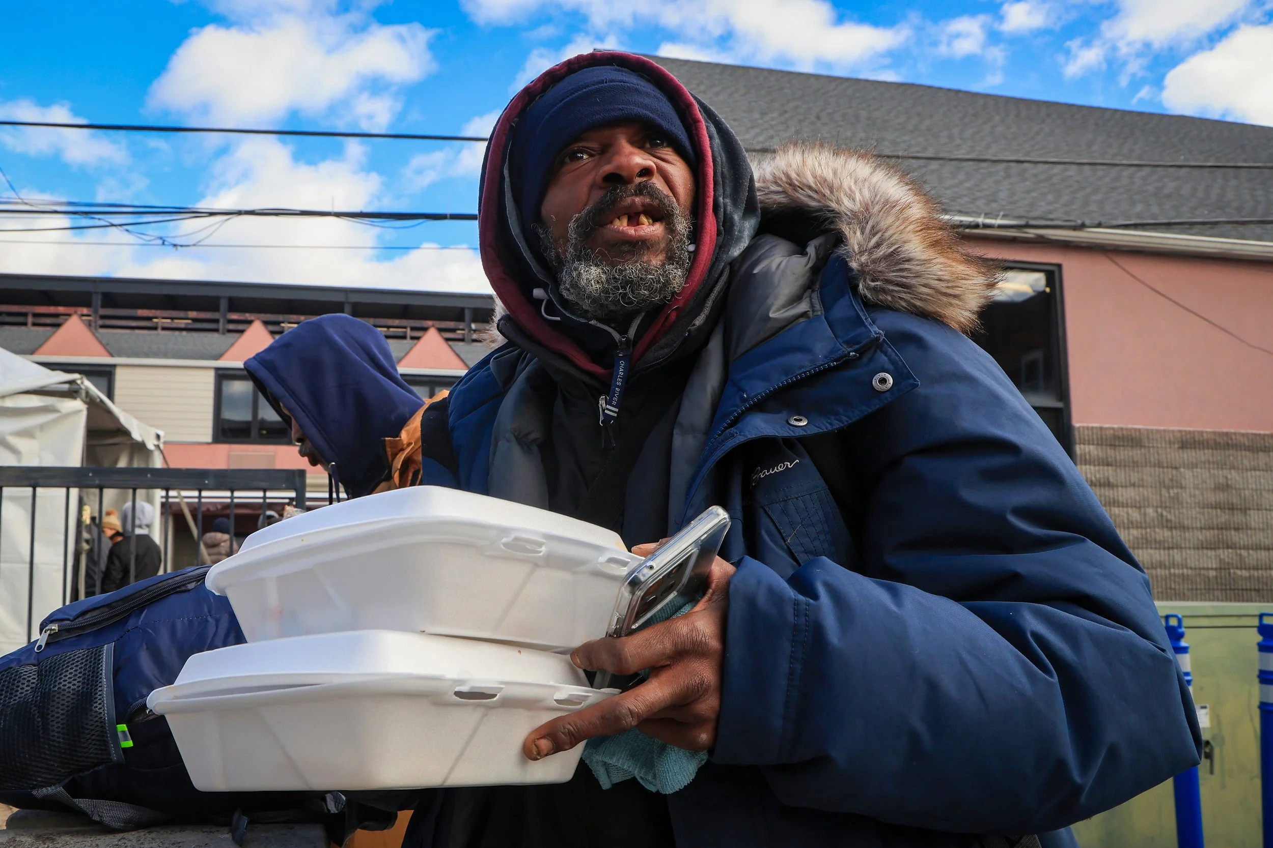 PATERSON, N.J. | Nov. 28, 2025: TK McKinnon, who says he identifies as homeless,  takes home boxes of food as student volunteers distribute sandwiches outside Eva’s Village in Paterson. Volunteers from the Paterson Youth Council, JFK High School Robo