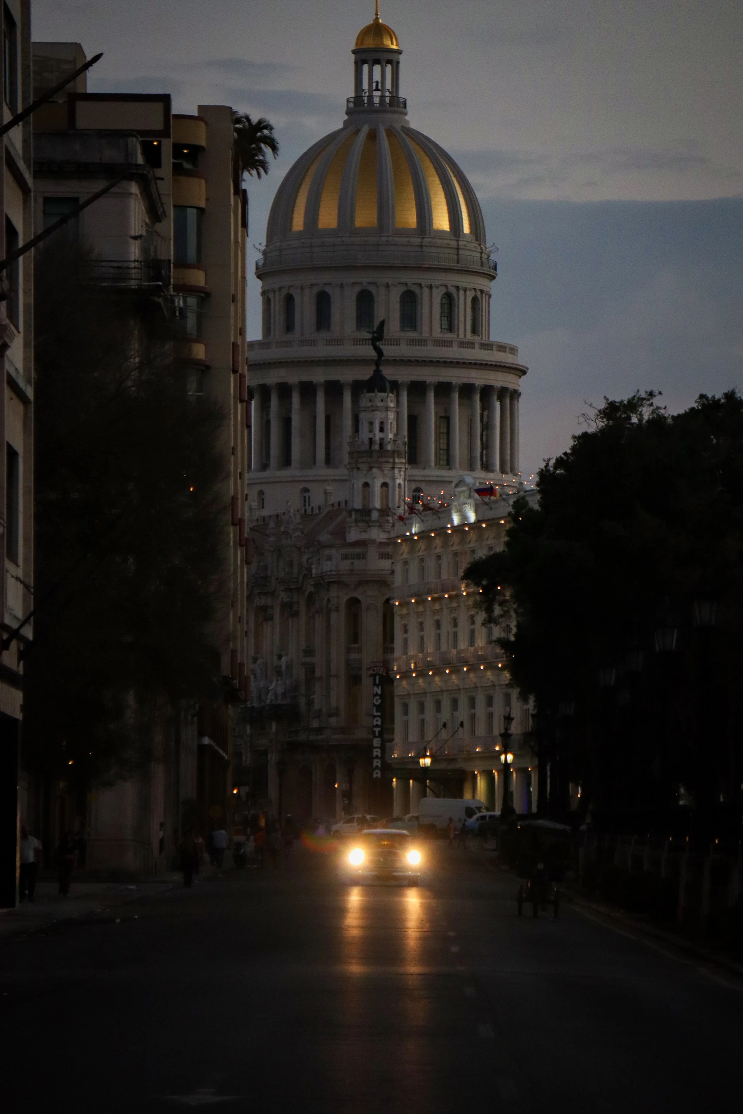 HAVANA, CUBA — March 9, 2026: Headlights from classic American cars cut through a dimly lit street as the dome of the Capitol (El Capitolio) rises in the background.