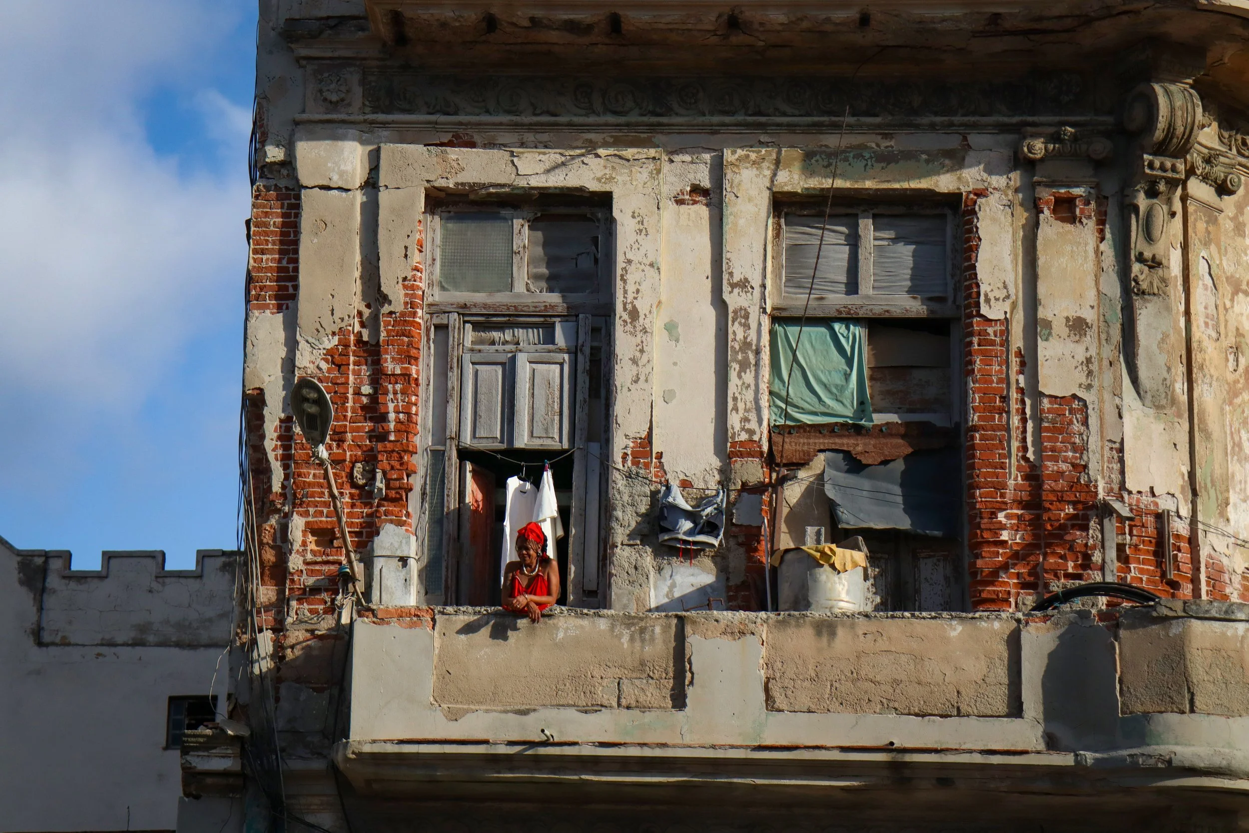HAVANA, CUBA — March 8, 2026: A woman stands on her balcony in Central Havana (Centro Habana), looking down at the street below, as the windows of her apartment are boarded up and patched with towels and tar paper