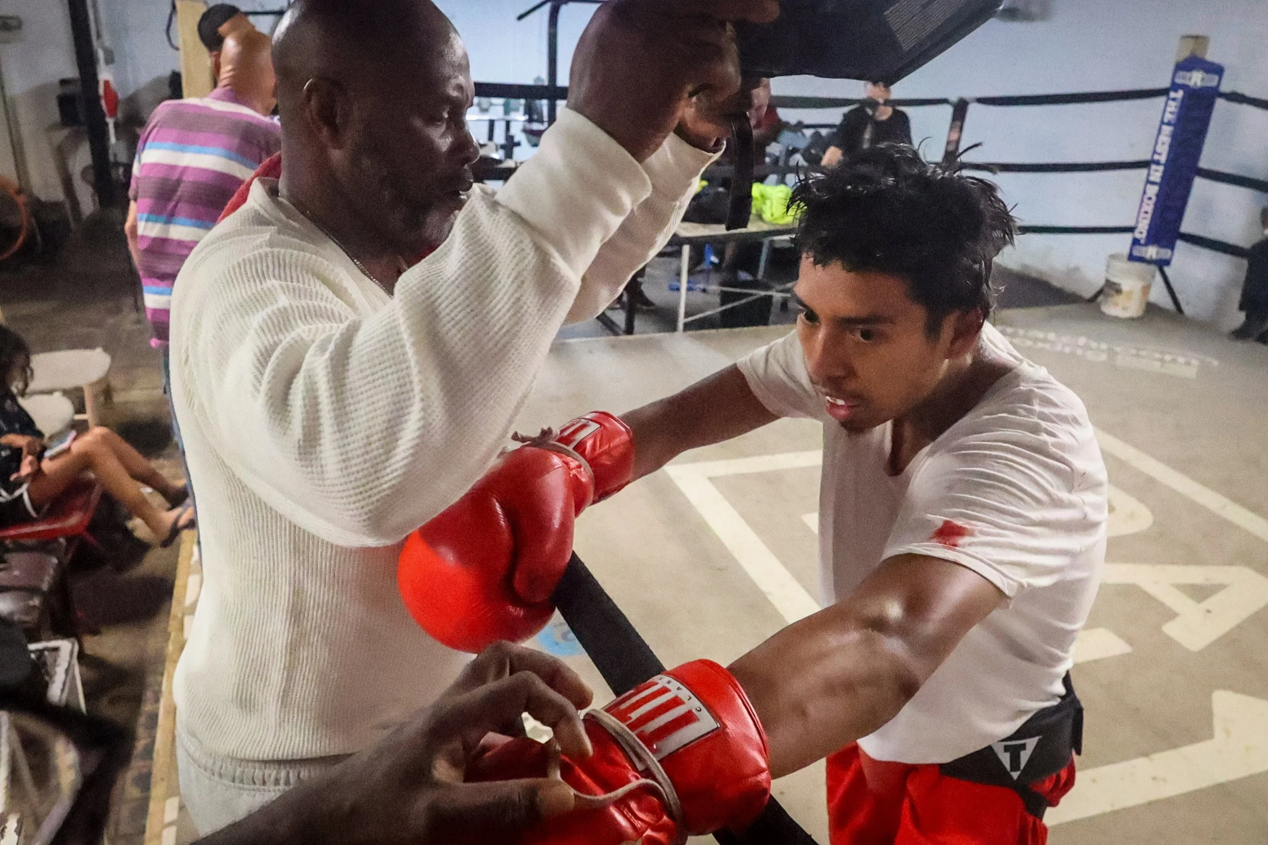 Trainer Ron Rasul Bacote helps fighter Erik Mendez take off his headgear after sparring